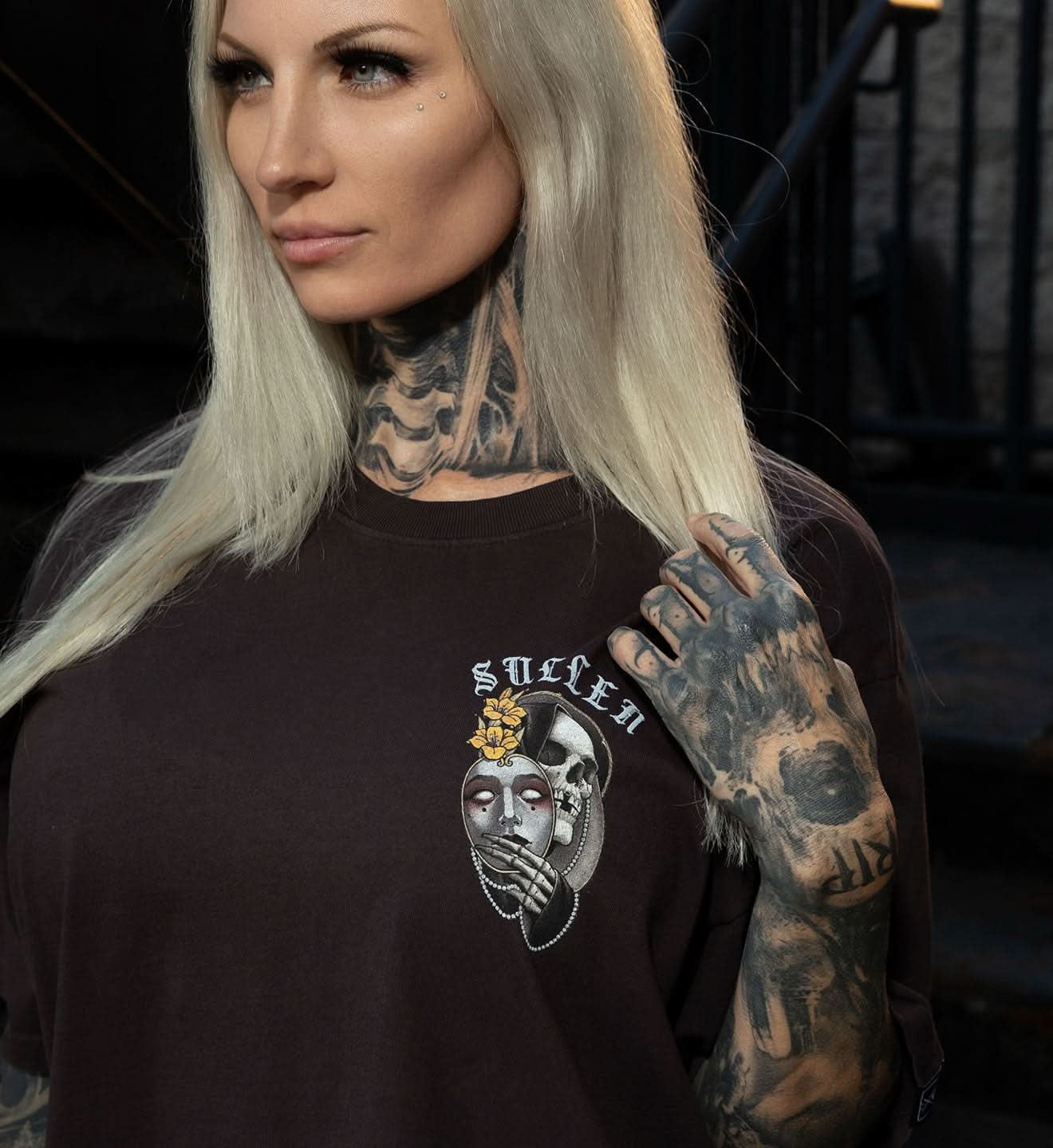 Person wearing a black t-shirt with a graphic design, standing against a dark background.