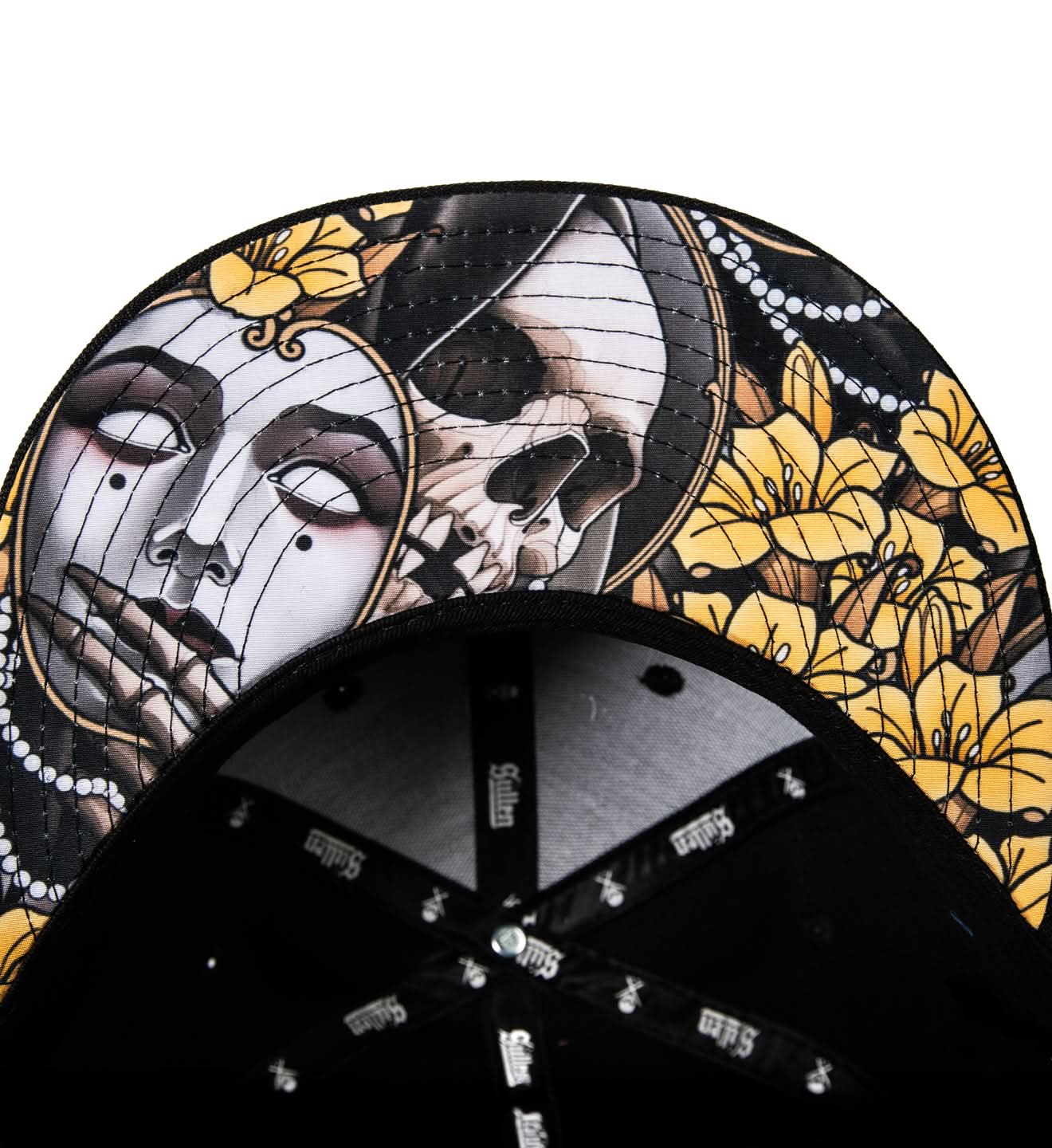 Black cap with a decorative design featuring a face, skull, and yellow flowers on a white background.