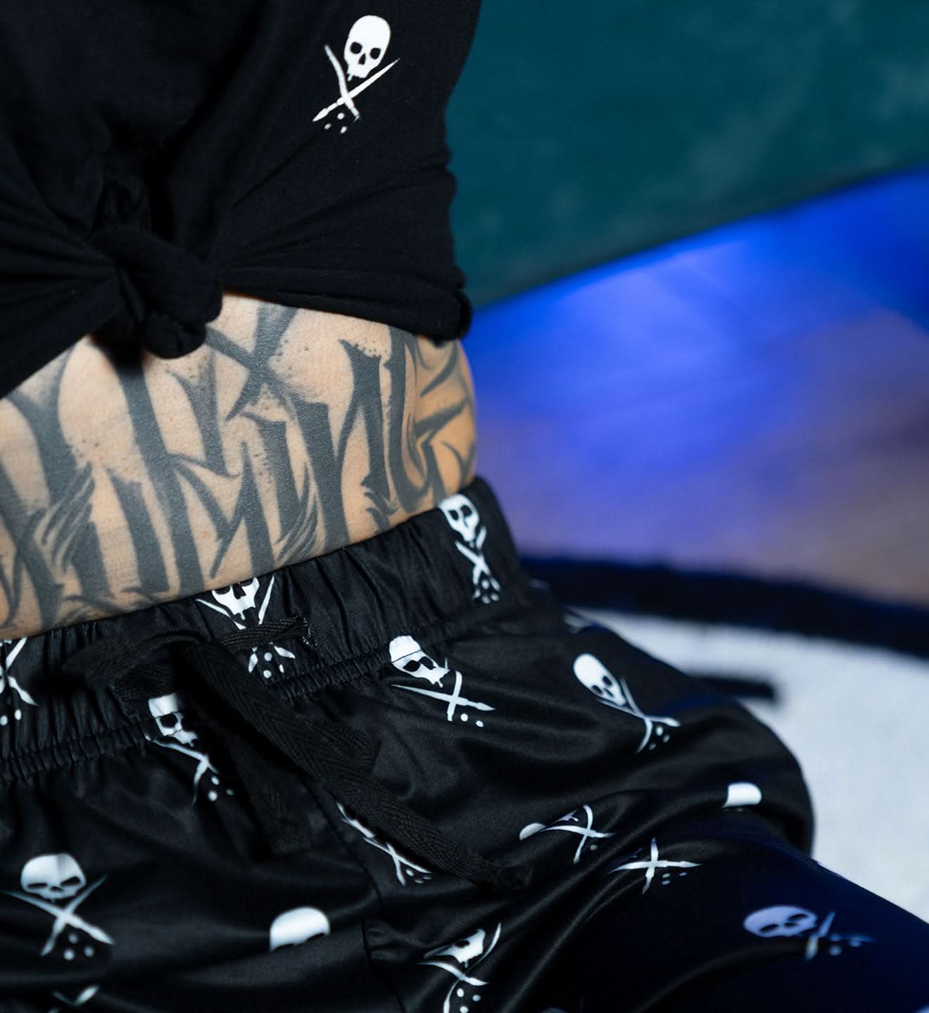 Person wearing black shorts with skull and crossbones pattern against a blurred background