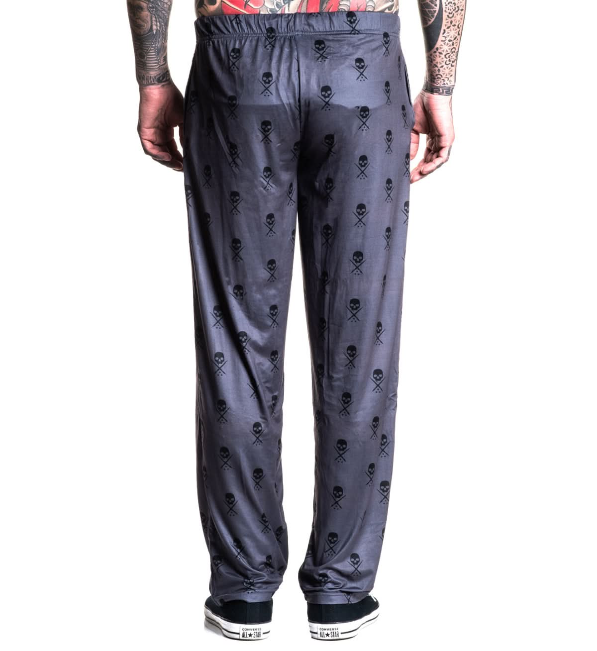 Gray sweatpants with skull and crossbones pattern worn by a person on a white background