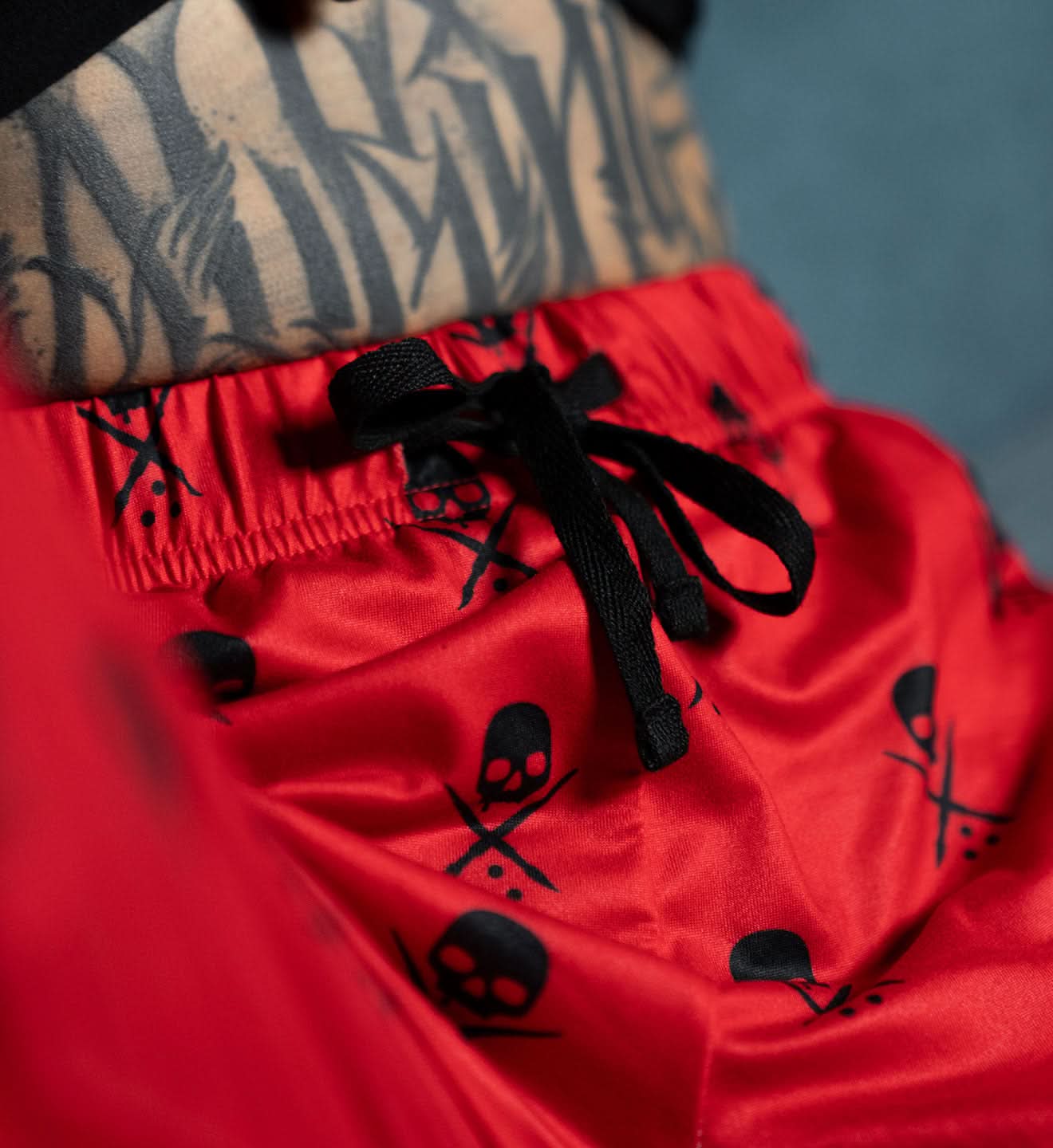 Red shorts with black skull designs and a tattooed arm in the background