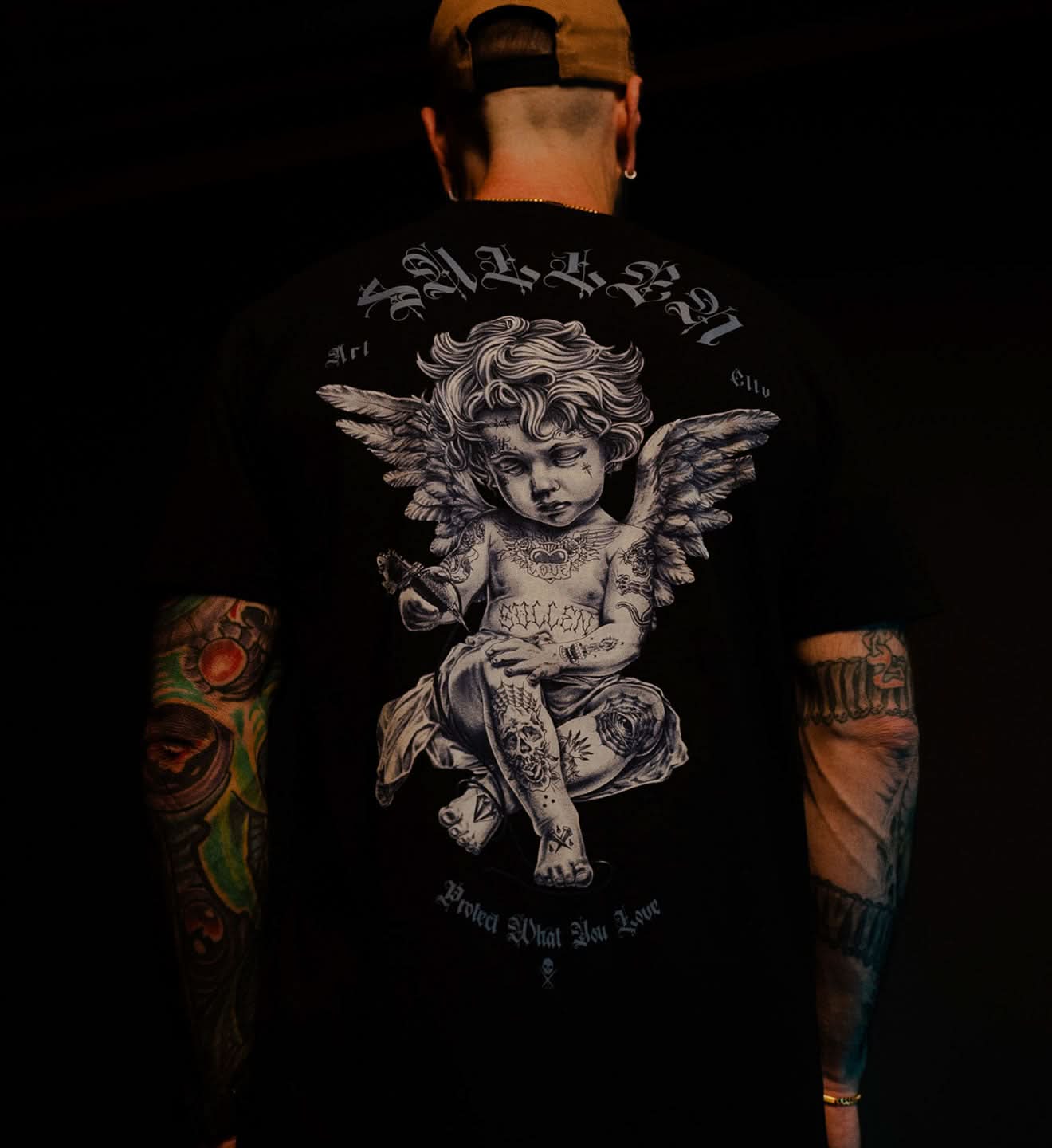 Person wearing a black t-shirt with an angel design on the back, standing against a dark background.