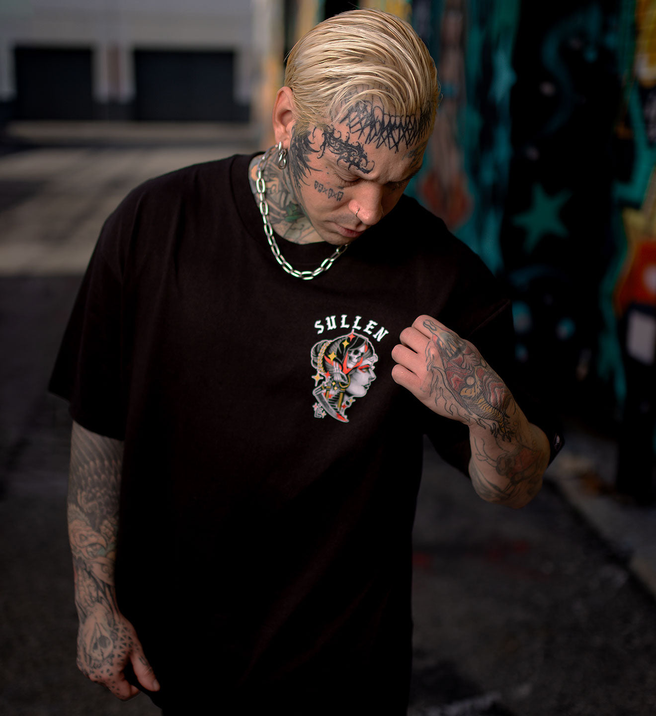 Person wearing a black Sullen t-shirt with tattoos visible on arms and neck.