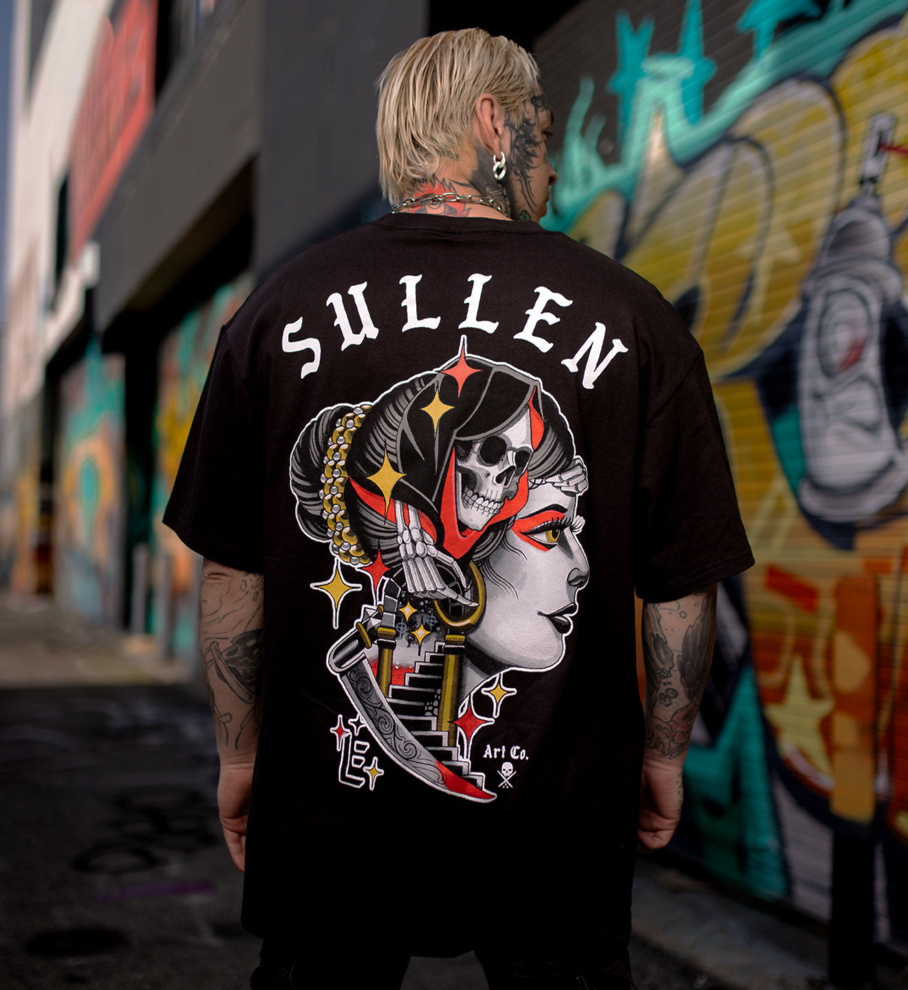 Person wearing a black Sullen t-shirt with a graphic design in an urban setting.