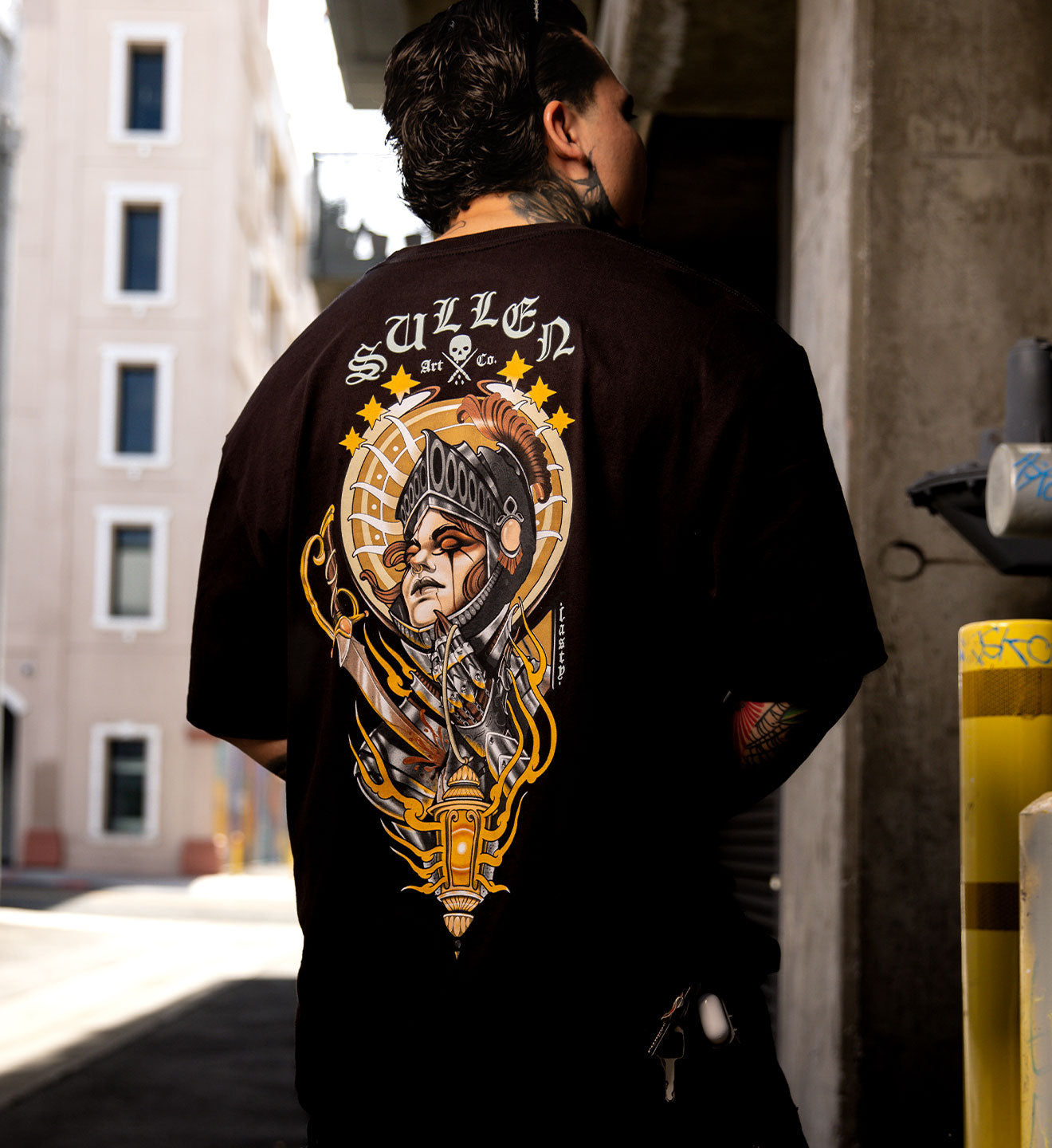 Person wearing a black t-shirt with a detailed graphic design on the back, standing in an urban setting.