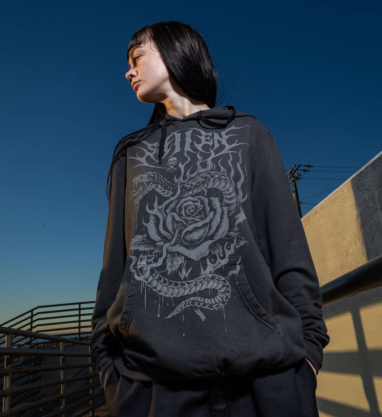 Person wearing a black hoodie with a graphic design against a blue sky.