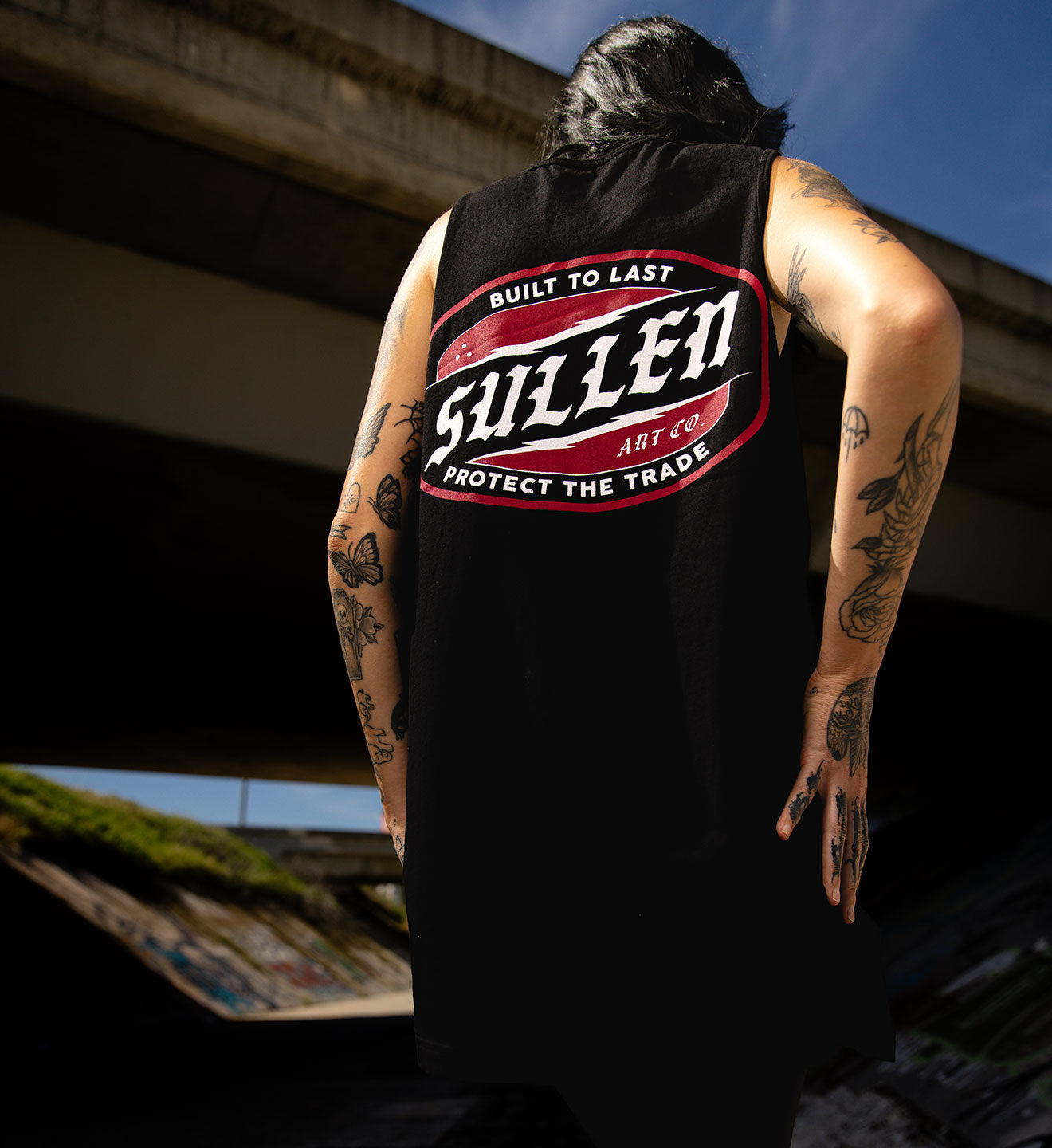 Person wearing a black sleeveless shirt with 'Sullen' logo outdoors.