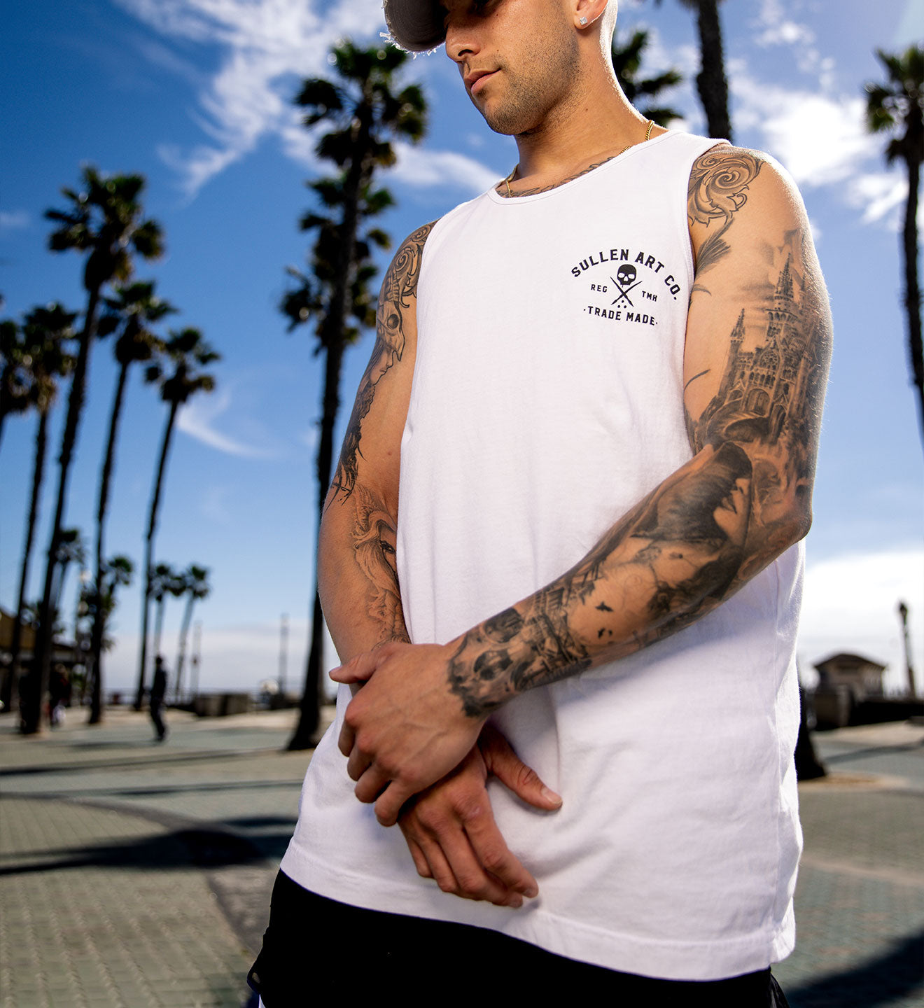 Man wearing a white t-shirt with a logo in front of palm trees
