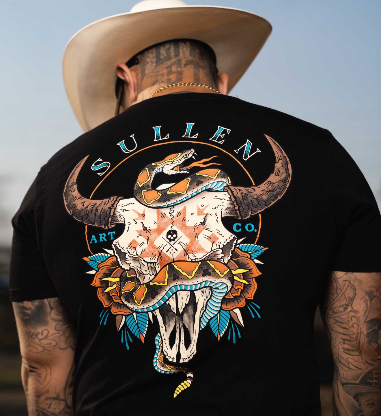 Person wearing a black Sullen Art Co. t-shirt with a bull skull design outdoors.