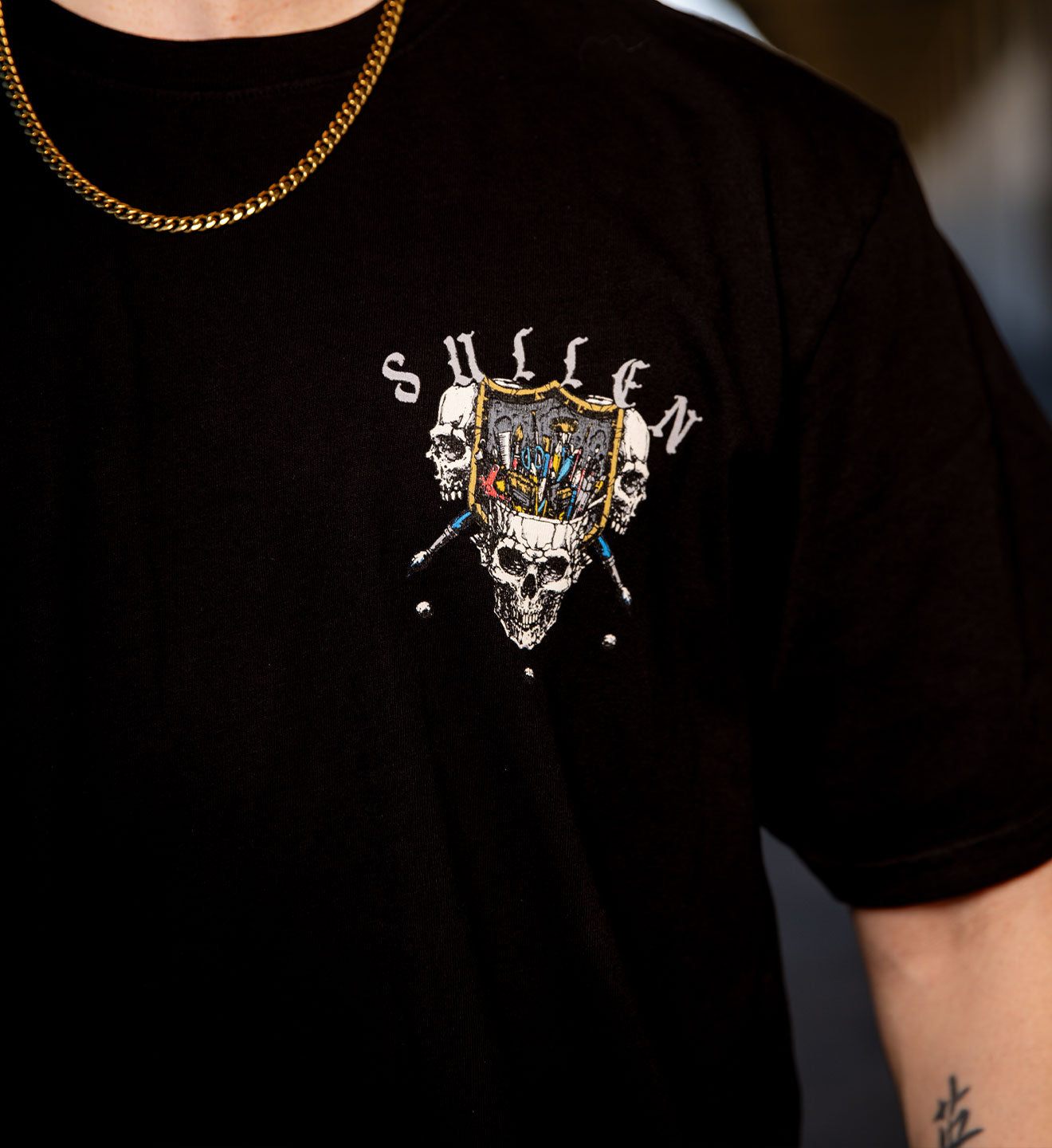 Black t-shirt with a skull and crossbones design and 'Sullen' branding.