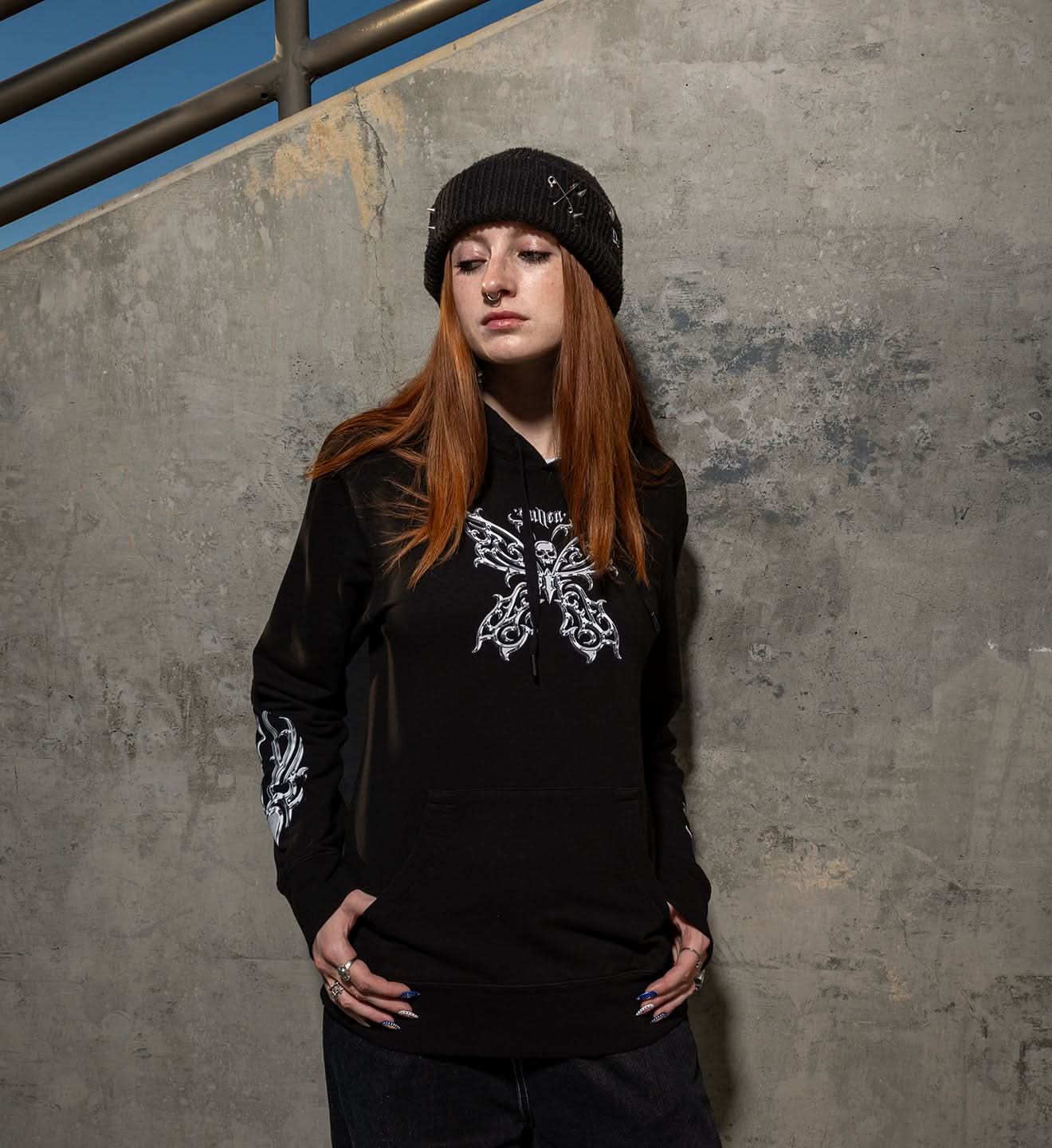 Person wearing a black hoodie with white designs against a concrete wall.