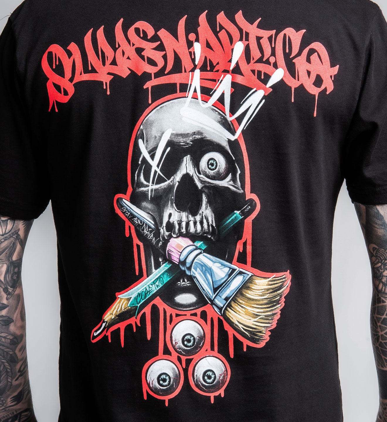 Black t-shirt with a graphic design featuring a skull, paintbrush, and tattoo needles on a white background.