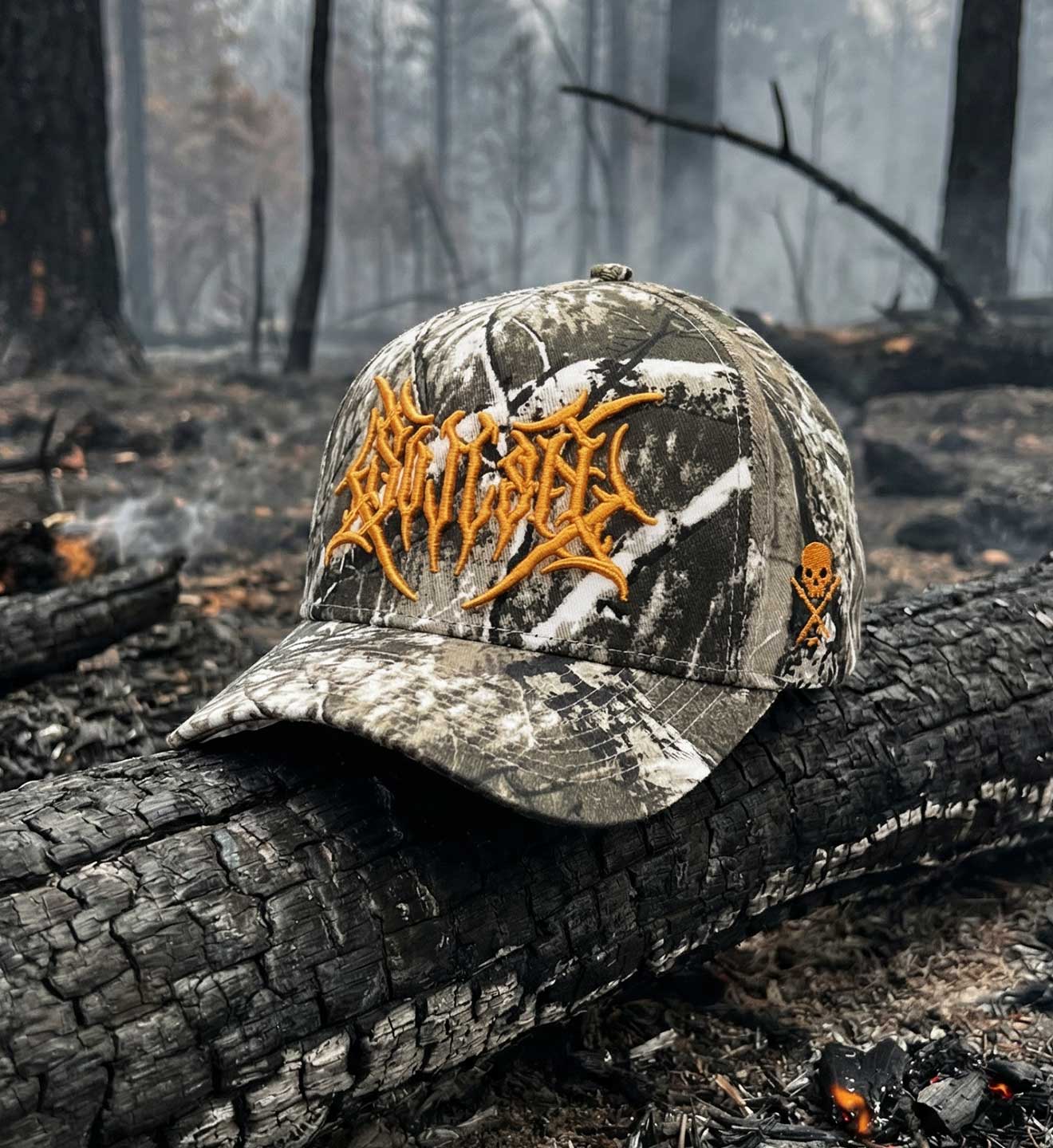 Camouflage cap with orange logo on a burnt log in a forest setting