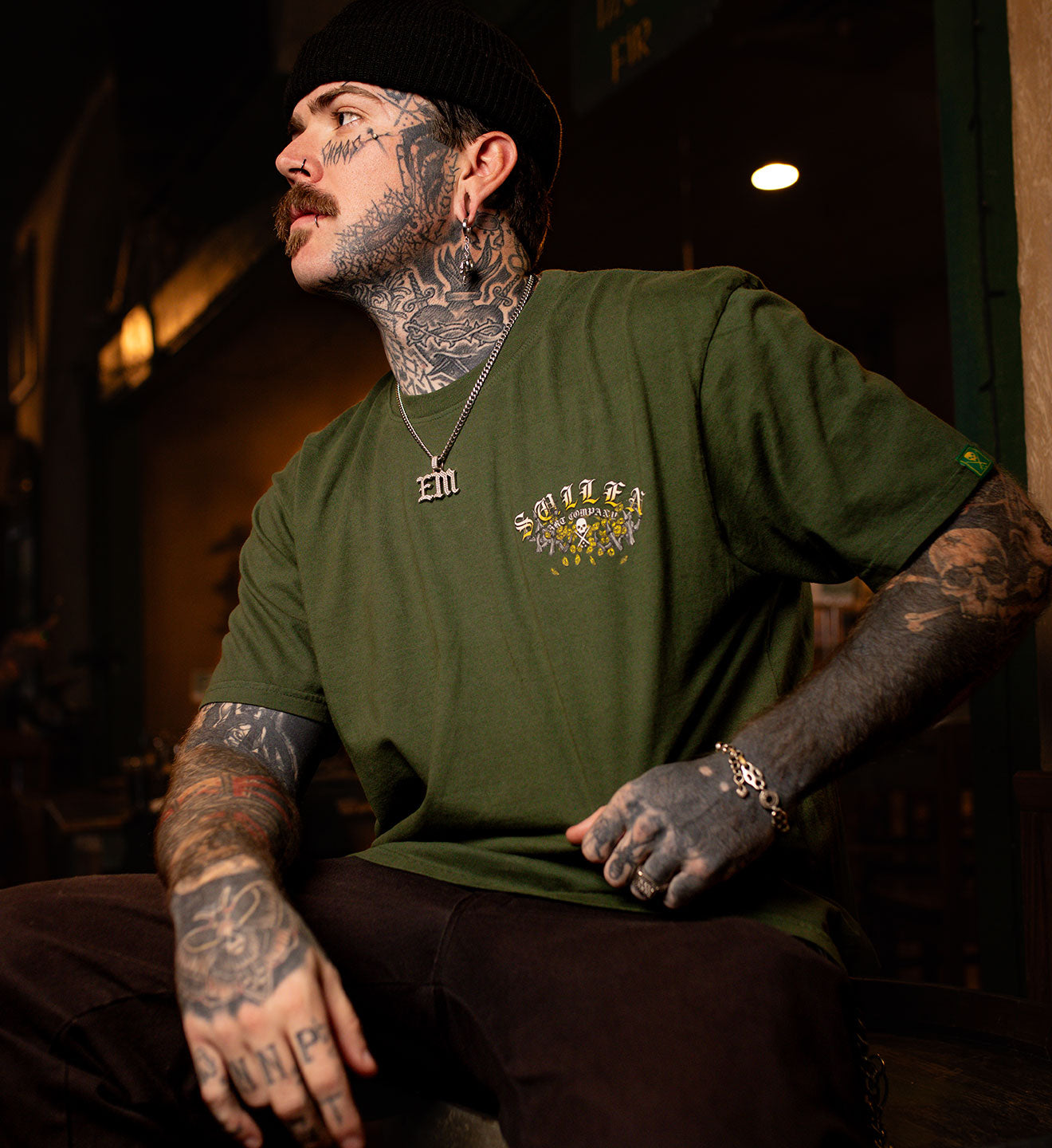 Man wearing a green t-shirt with a colorful graphic design, sitting indoors.