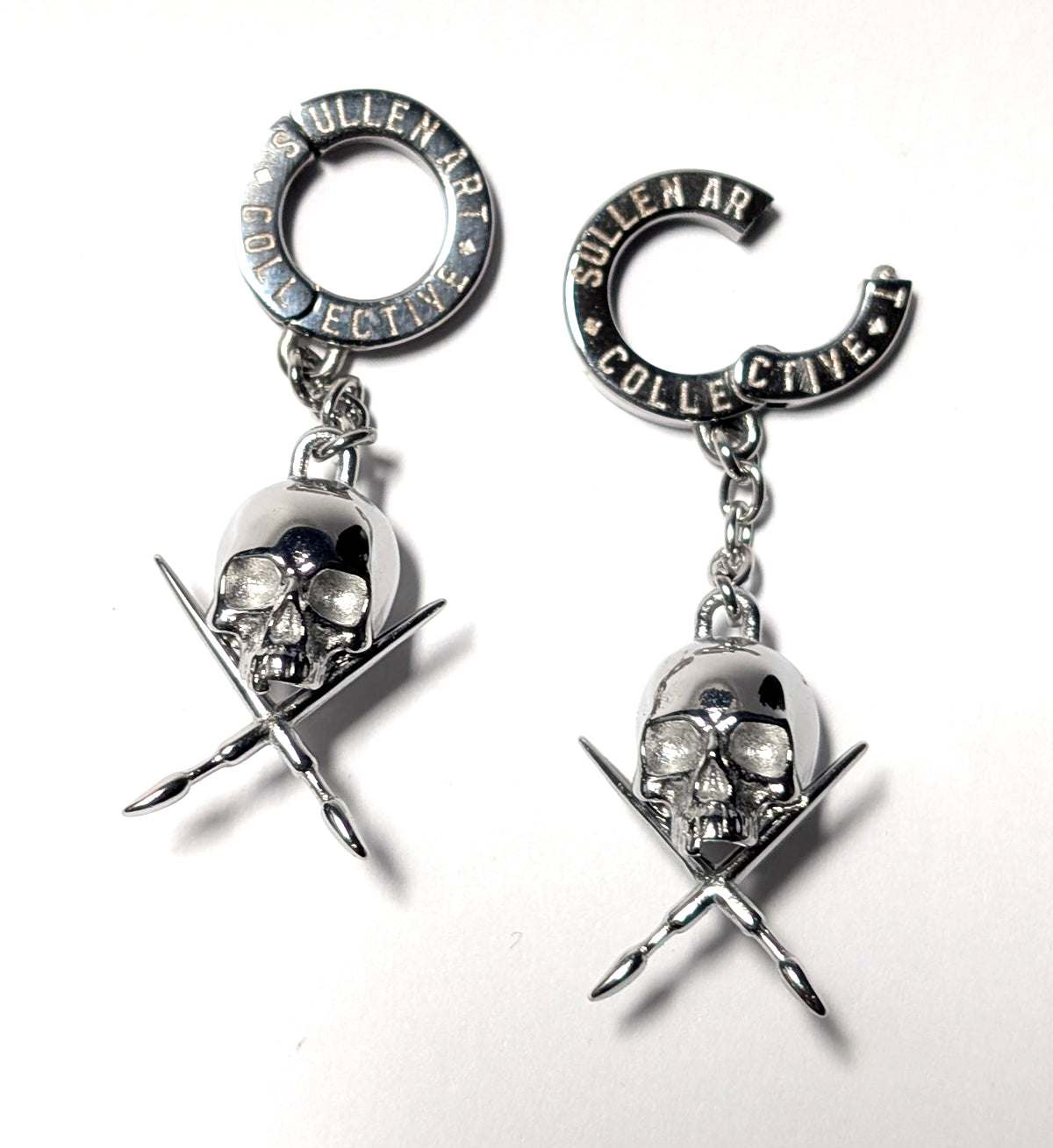 Pair of earrings with skull and crossbar design on a white background