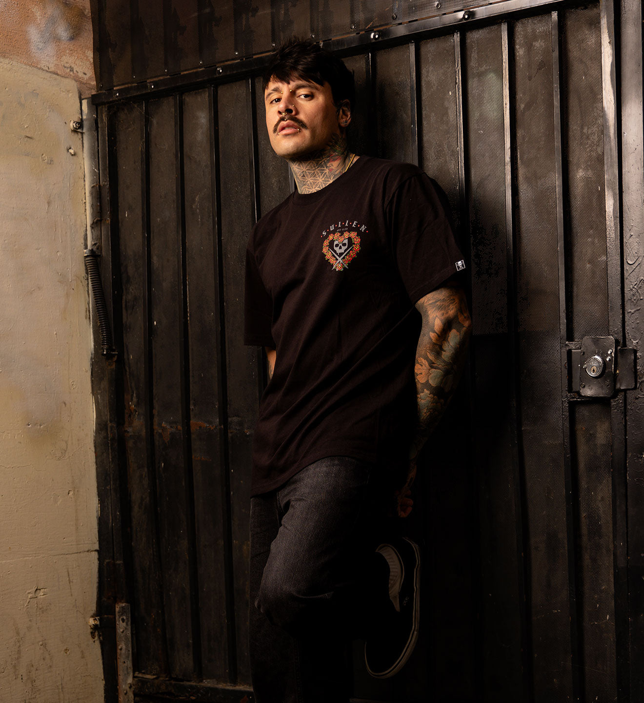 BLACK SULLEN T SHIRT WITH A SOFT GRAPHITE PORTRAIT OF A FEMALE TATTOOER FRAMED WITH TRADITIONAL COLORED ROSES IN THE SHAPE OF A HEART 