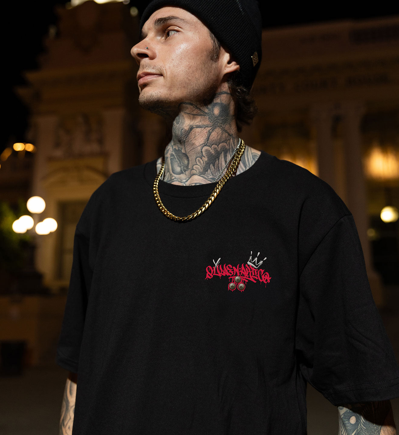 Man wearing a black t-shirt with a red logo and text, standing outdoors at night.