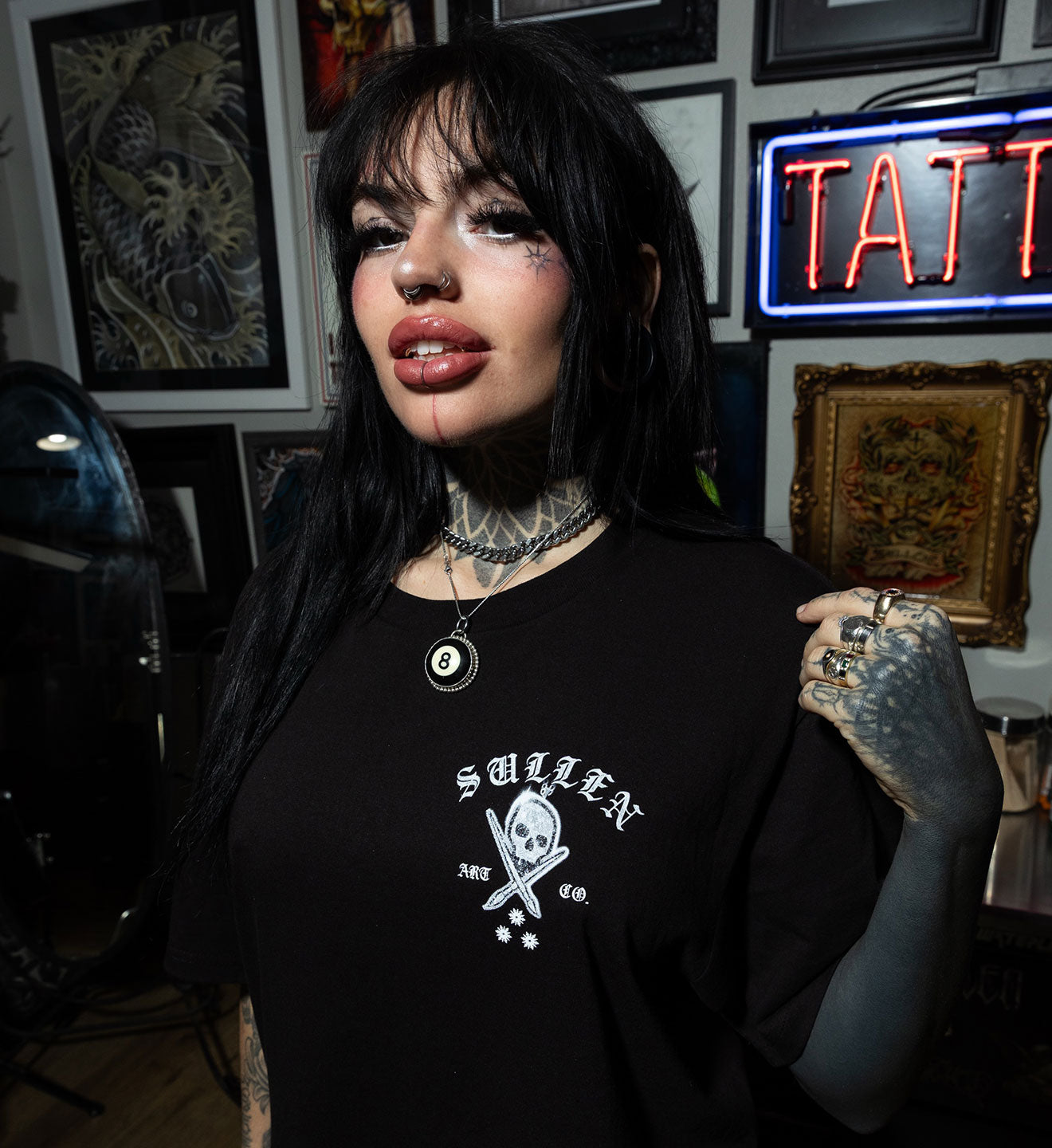 Person wearing a black t-shirt with a logo in an tattoo parlor setting