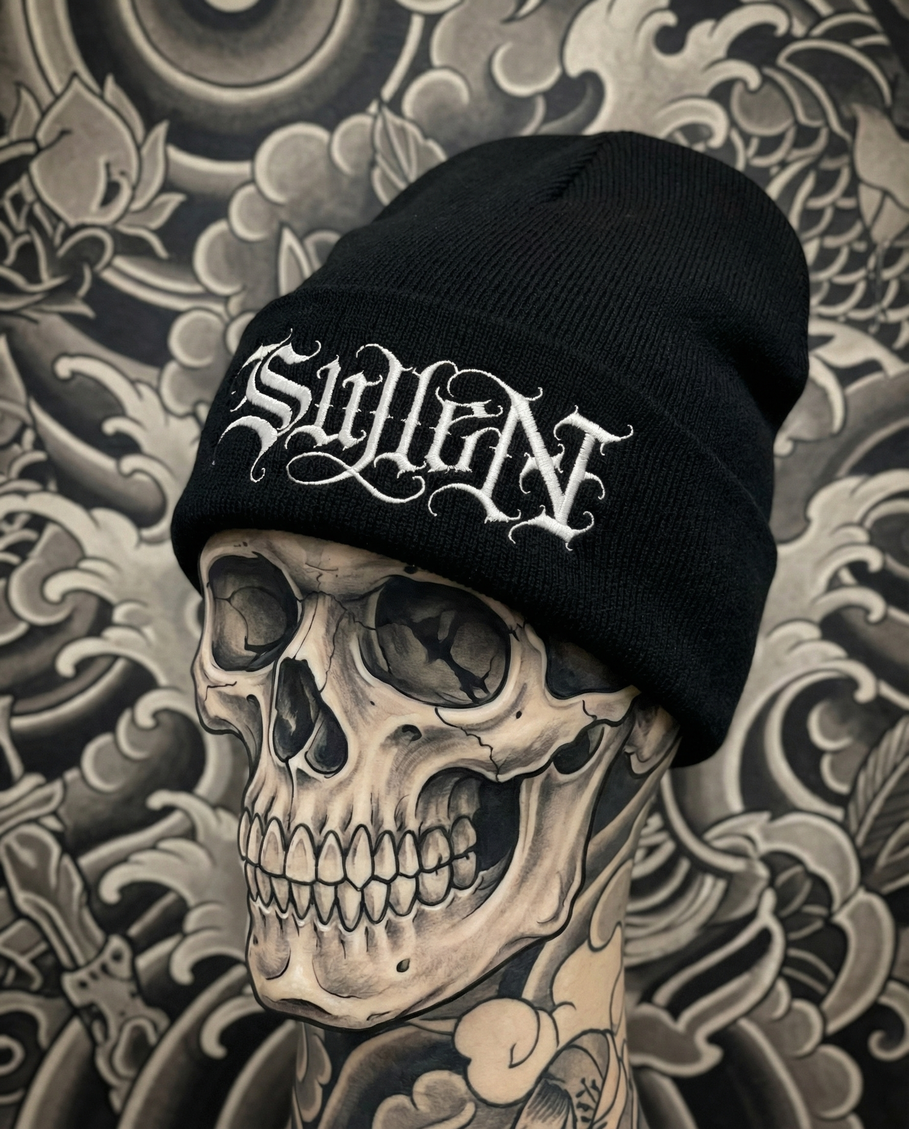 Black beanie with 'Sicilian' text on a skull and tattooed arm against a patterned background