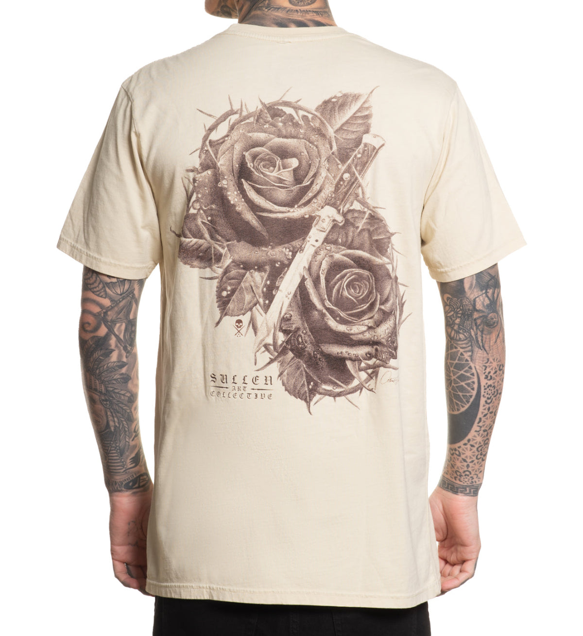 Beige t-shirt with rose and cross design on the back, worn by a person with tattoos.