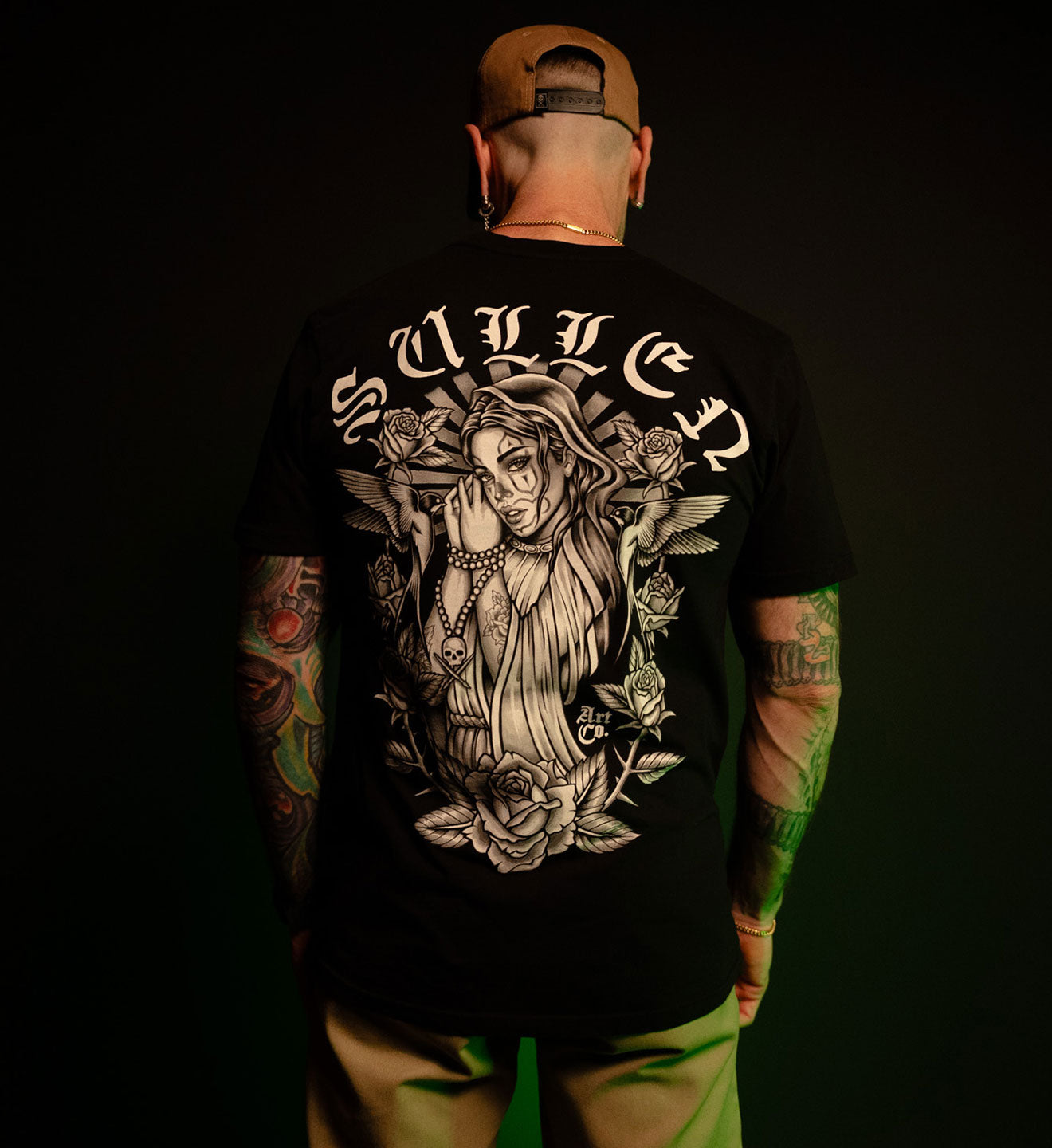 Person wearing a black t-shirt with a graphic design and 'Sullen' branding on the back, against a dark background.