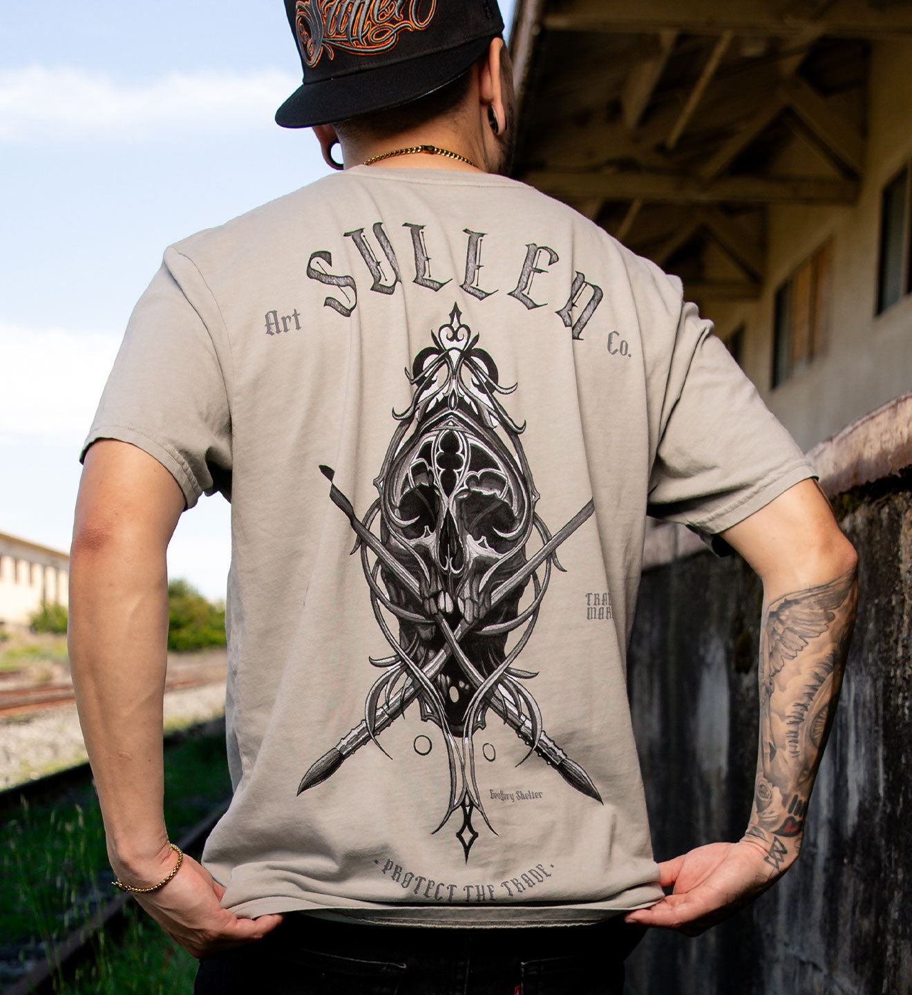 Person wearing a 'Sullen' t-shirt with a graphic design on the back, standing outdoors.